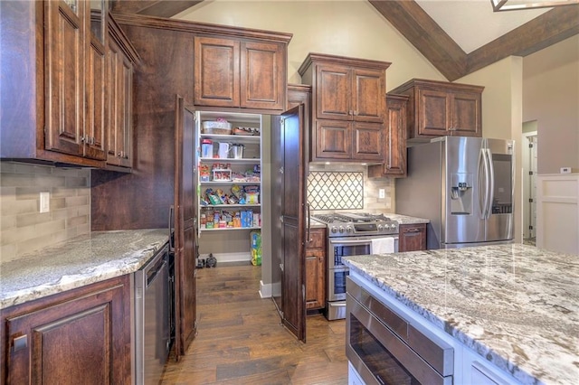 kitchen with lofted ceiling, appliances with stainless steel finishes, dark hardwood / wood-style flooring, light stone countertops, and decorative backsplash