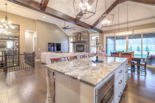 kitchen featuring white cabinetry, hanging light fixtures, a center island, light stone countertops, and dark wood-type flooring