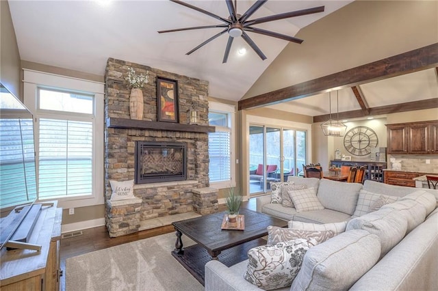 living room with dark hardwood / wood-style flooring, vaulted ceiling with beams, a stone fireplace, and a healthy amount of sunlight