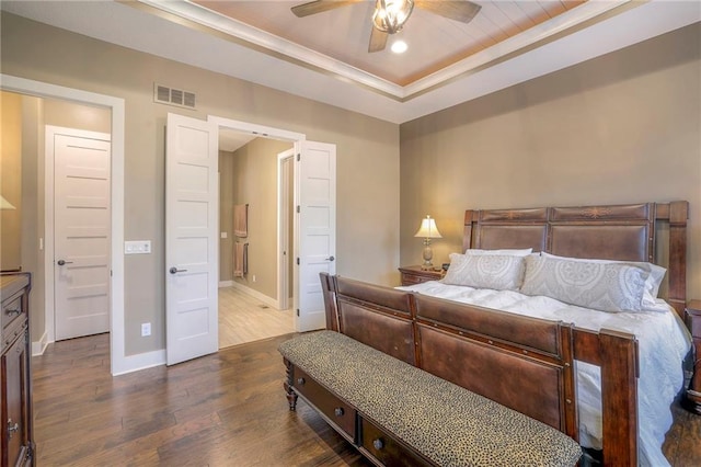 bedroom featuring hardwood / wood-style flooring, ceiling fan, connected bathroom, and a tray ceiling