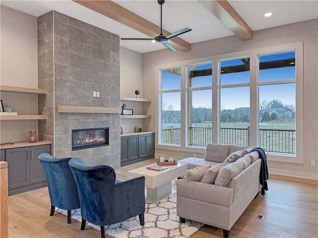 living room featuring ceiling fan, beam ceiling, a tile fireplace, and light wood-type flooring