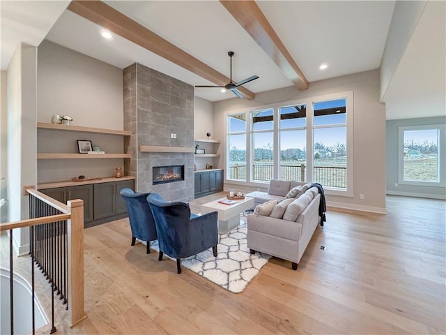 living room featuring beam ceiling, ceiling fan, a fireplace, and light hardwood / wood-style floors