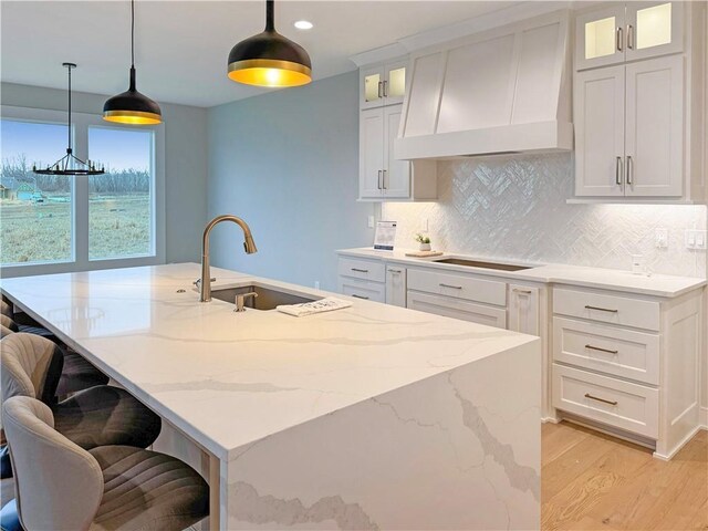 kitchen with pendant lighting, a center island with sink, custom exhaust hood, and white cabinets