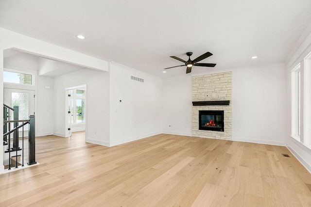 unfurnished living room featuring light hardwood / wood-style flooring, a wealth of natural light, ceiling fan, and a stone fireplace