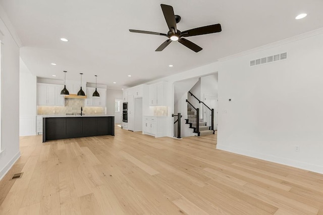 unfurnished living room featuring light wood-type flooring, ceiling fan, sink, and crown molding