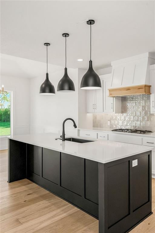 kitchen featuring pendant lighting, sink, light hardwood / wood-style flooring, white cabinetry, and a spacious island