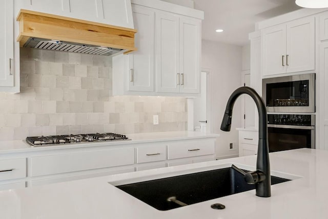 kitchen featuring backsplash, custom exhaust hood, stainless steel appliances, and white cabinets