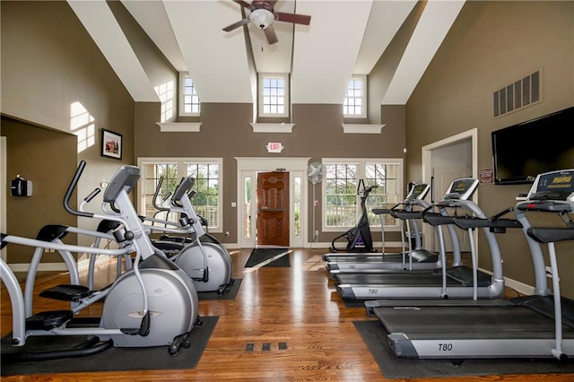 gym featuring a towering ceiling, ceiling fan, and dark hardwood / wood-style flooring