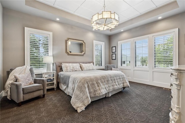 bedroom with a raised ceiling, a notable chandelier, and dark colored carpet