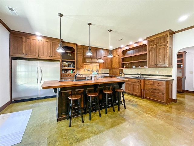 kitchen featuring backsplash, a center island with sink, hanging light fixtures, stainless steel fridge, and butcher block counters