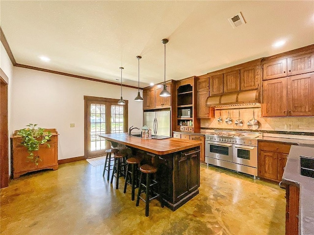 kitchen featuring decorative backsplash, appliances with stainless steel finishes, a breakfast bar, a kitchen island with sink, and hanging light fixtures