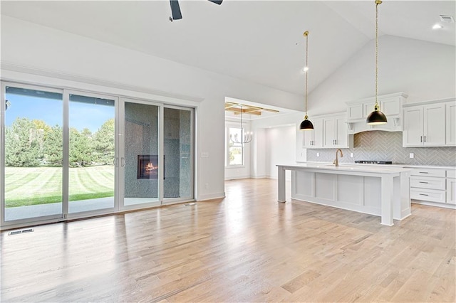 kitchen with light hardwood / wood-style floors, white cabinetry, high vaulted ceiling, pendant lighting, and a center island with sink