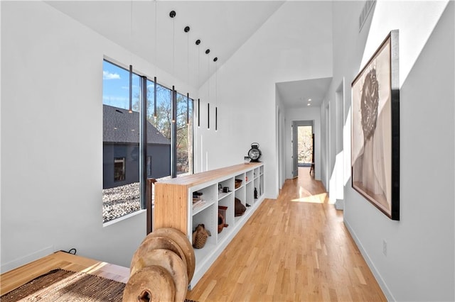 hall with high vaulted ceiling, a healthy amount of sunlight, and light hardwood / wood-style floors