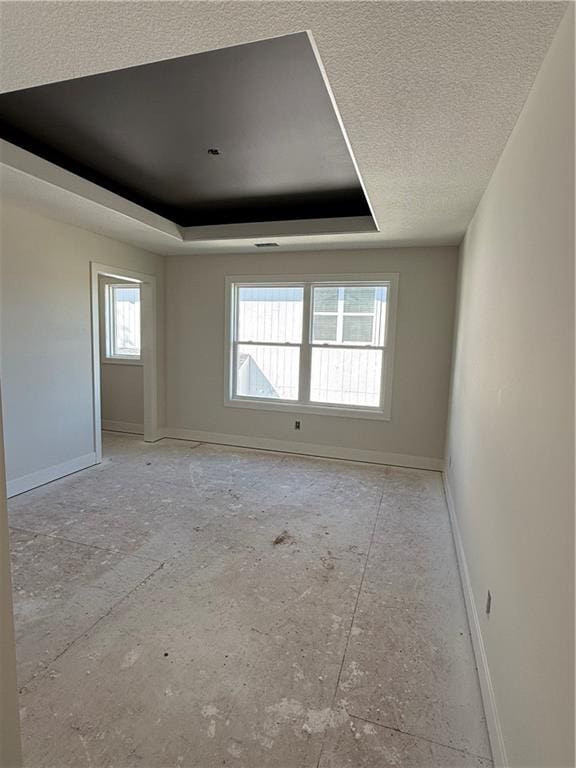 empty room with a raised ceiling, a textured ceiling, and a wealth of natural light