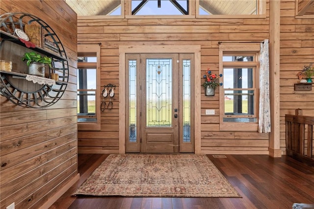 foyer featuring high vaulted ceiling, dark wood-type flooring, and wooden walls