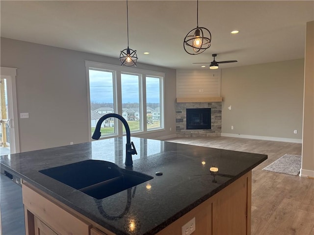 kitchen featuring decorative light fixtures, an island with sink, sink, dark stone countertops, and light hardwood / wood-style flooring