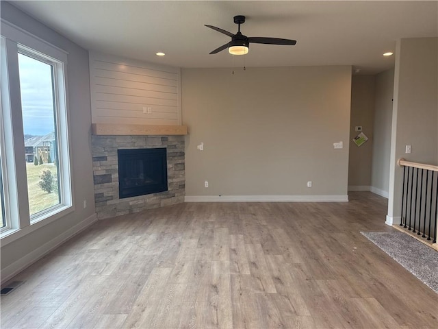 unfurnished living room with ceiling fan, a stone fireplace, and light wood-type flooring