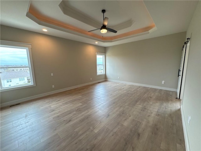 empty room featuring a raised ceiling, a barn door, light wood-type flooring, and ceiling fan