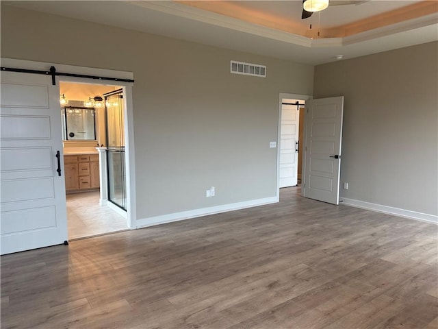 unfurnished room with a barn door, hardwood / wood-style floors, ceiling fan, and a tray ceiling