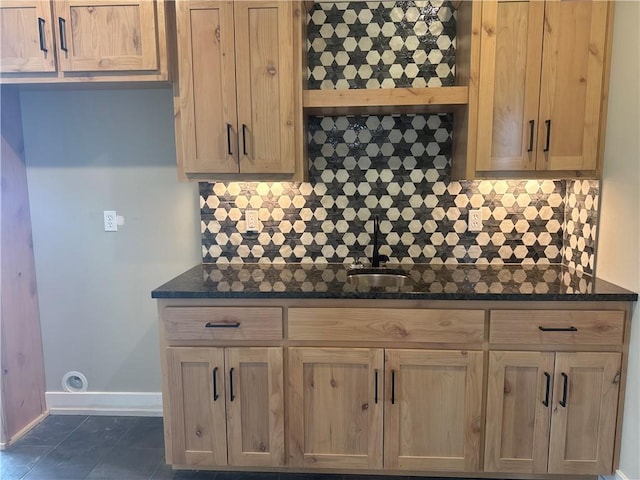 kitchen featuring backsplash, dark tile patterned flooring, sink, and dark stone countertops