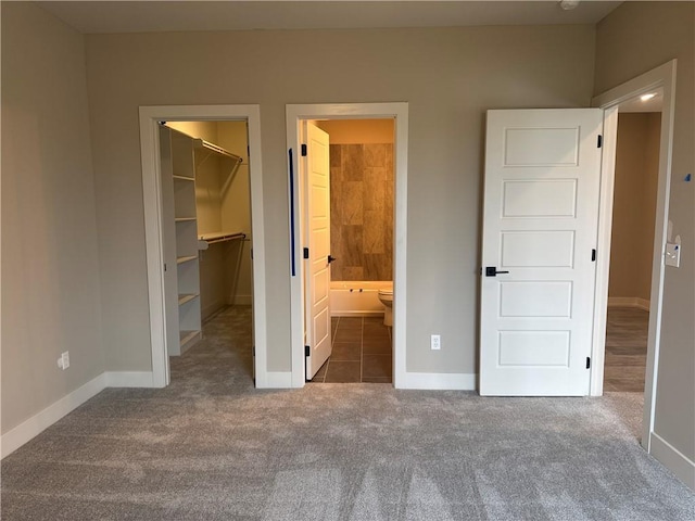 unfurnished bedroom featuring connected bathroom, a spacious closet, a closet, and dark colored carpet