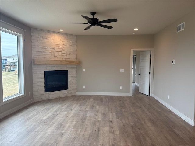 unfurnished living room with hardwood / wood-style floors, a stone fireplace, and ceiling fan