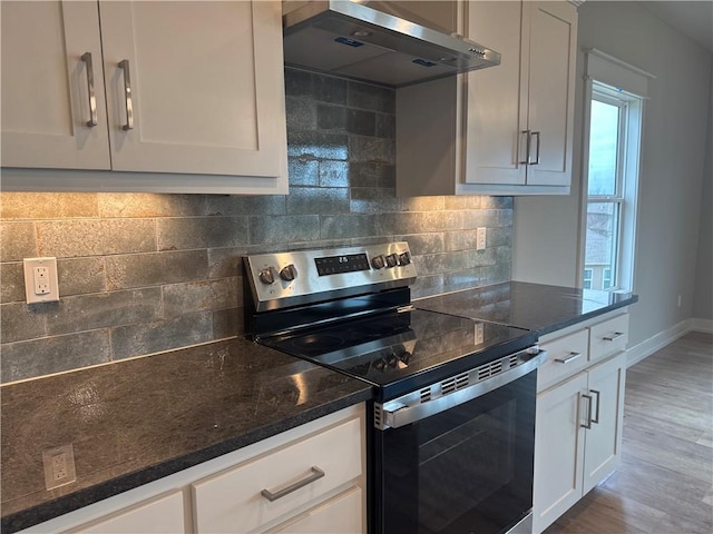 kitchen featuring stainless steel range with electric stovetop, white cabinetry, exhaust hood, and dark stone countertops