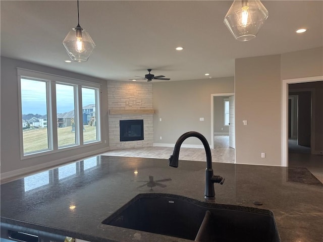 kitchen featuring sink, decorative light fixtures, dark stone countertops, ceiling fan, and a fireplace