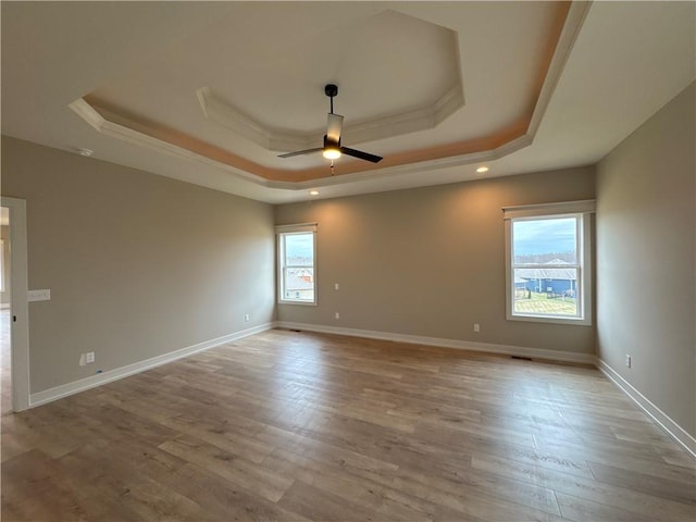 unfurnished room with ceiling fan, light wood-type flooring, and a tray ceiling