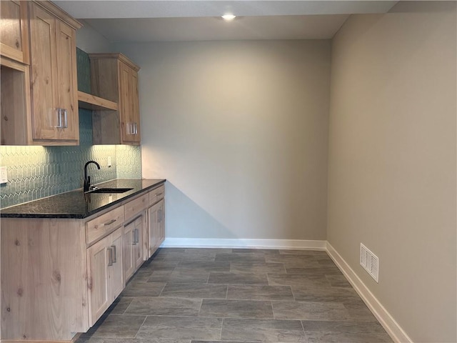 kitchen featuring sink, decorative backsplash, light brown cabinetry, and dark stone counters