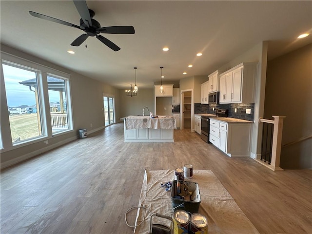 kitchen featuring backsplash, stainless steel appliances, white cabinets, a center island with sink, and decorative light fixtures