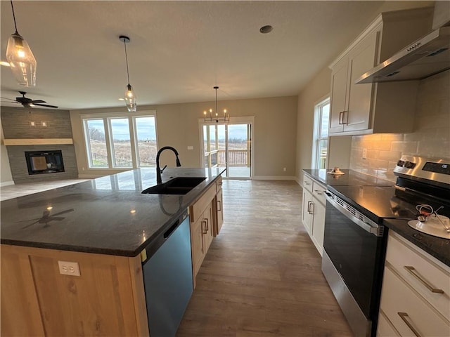 kitchen featuring wall chimney exhaust hood, sink, a center island with sink, stainless steel appliances, and white cabinets