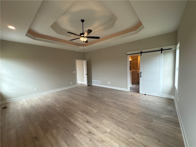 unfurnished bedroom featuring ensuite bathroom, hardwood / wood-style flooring, a raised ceiling, and a barn door