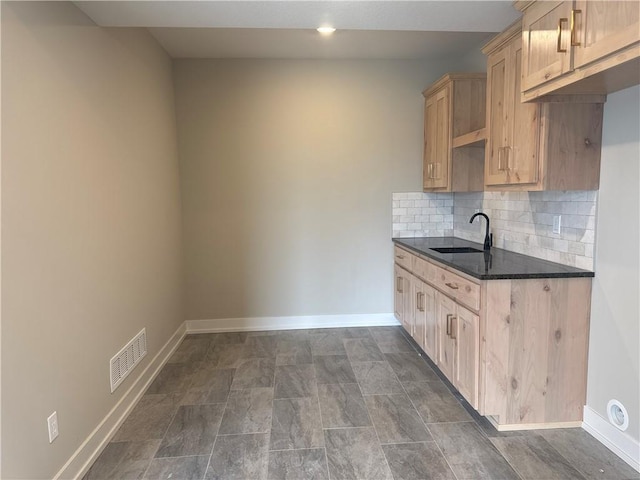 kitchen featuring tasteful backsplash, dark stone countertops, sink, and light brown cabinets