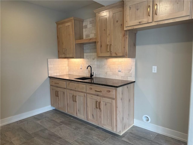 kitchen featuring dark stone countertops, light brown cabinetry, sink, and backsplash