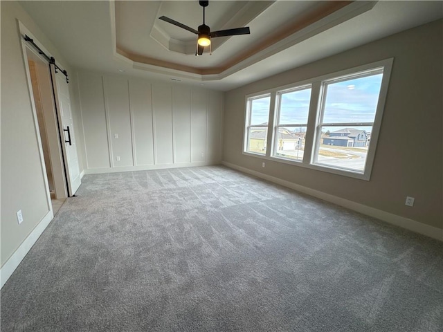 carpeted spare room featuring a tray ceiling, a barn door, and ceiling fan