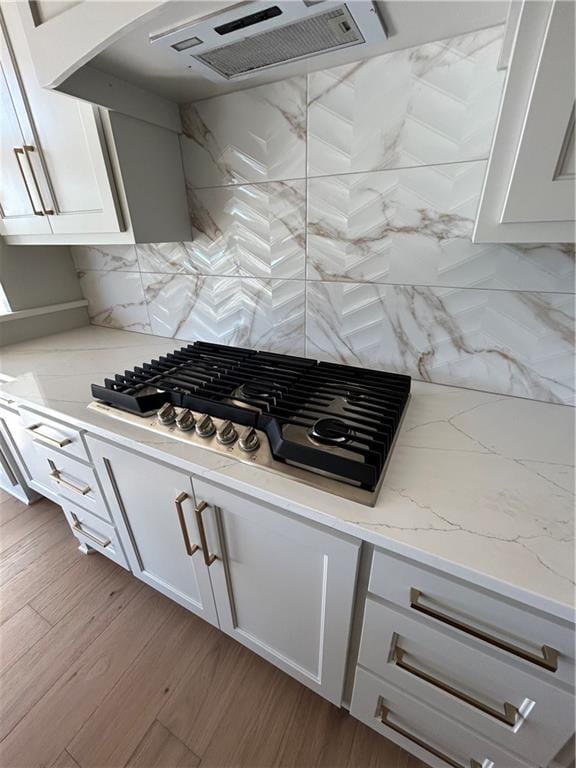 kitchen featuring light hardwood / wood-style floors, stainless steel gas cooktop, tasteful backsplash, exhaust hood, and light stone countertops