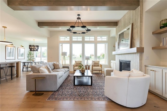 living room with beam ceiling, wood-type flooring, a chandelier, and a fireplace