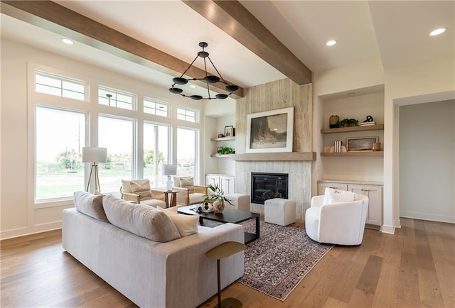 living room featuring a fireplace, beam ceiling, light wood-type flooring, and built in shelves