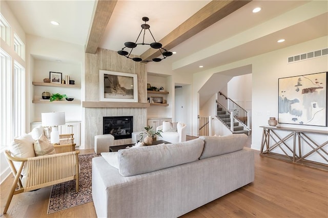 living room with a fireplace, beamed ceiling, a notable chandelier, and light wood-type flooring