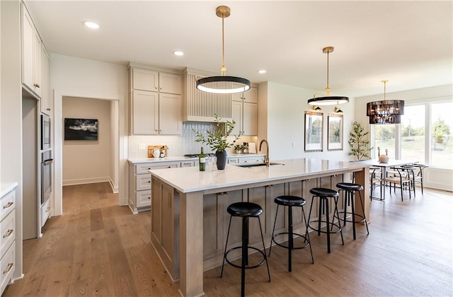 kitchen featuring hanging light fixtures, a center island with sink, hardwood / wood-style floors, a notable chandelier, and tasteful backsplash