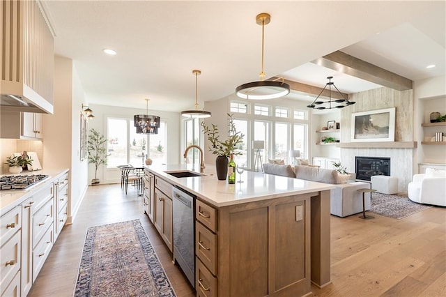 kitchen with sink, hanging light fixtures, beam ceiling, light hardwood / wood-style flooring, and a kitchen island with sink