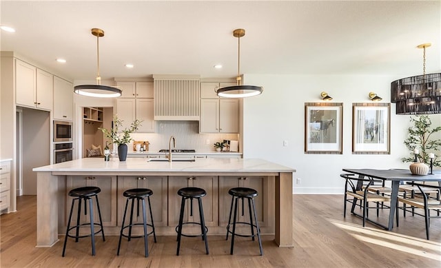 kitchen featuring a kitchen island with sink, light hardwood / wood-style flooring, hanging light fixtures, and stainless steel appliances