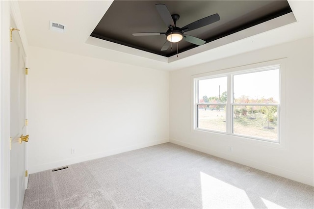 carpeted empty room featuring ceiling fan and a raised ceiling