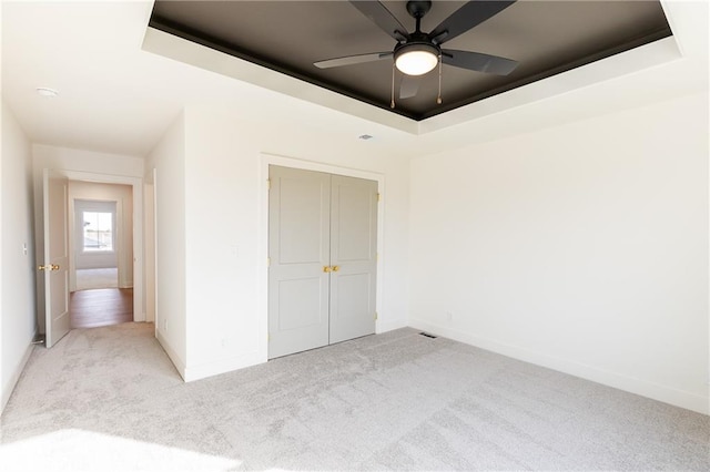 unfurnished bedroom with a closet, ceiling fan, light carpet, and a tray ceiling