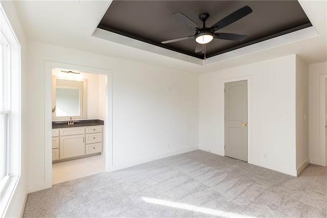 unfurnished bedroom featuring sink, light colored carpet, a raised ceiling, ensuite bathroom, and ceiling fan