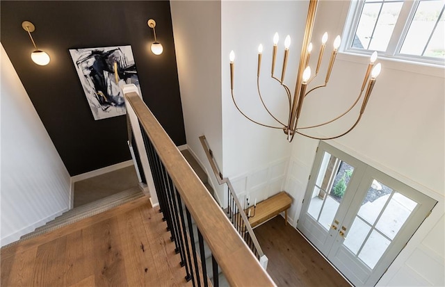 staircase featuring french doors, hardwood / wood-style flooring, and an inviting chandelier