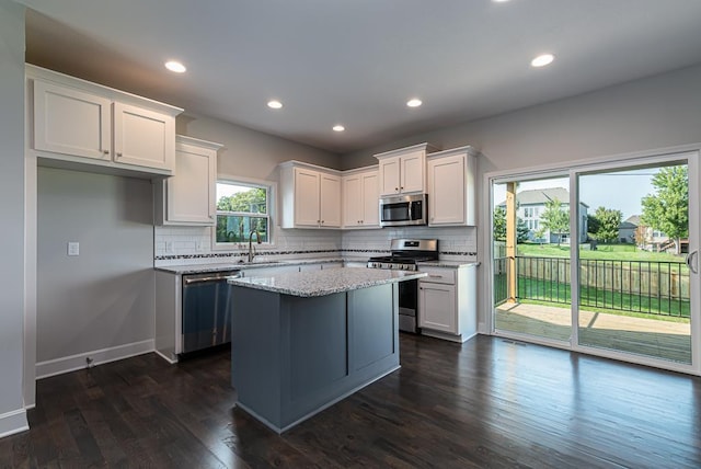 kitchen with tasteful backsplash, appliances with stainless steel finishes, white cabinetry, dark wood-type flooring, and a center island