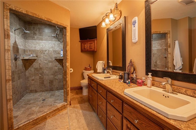 bathroom featuring tile patterned flooring, vanity, a tile shower, and toilet