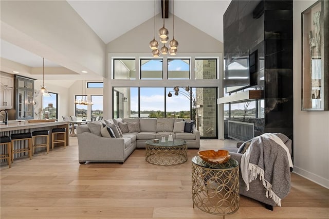 living room with an inviting chandelier, light hardwood / wood-style floors, high vaulted ceiling, and a healthy amount of sunlight